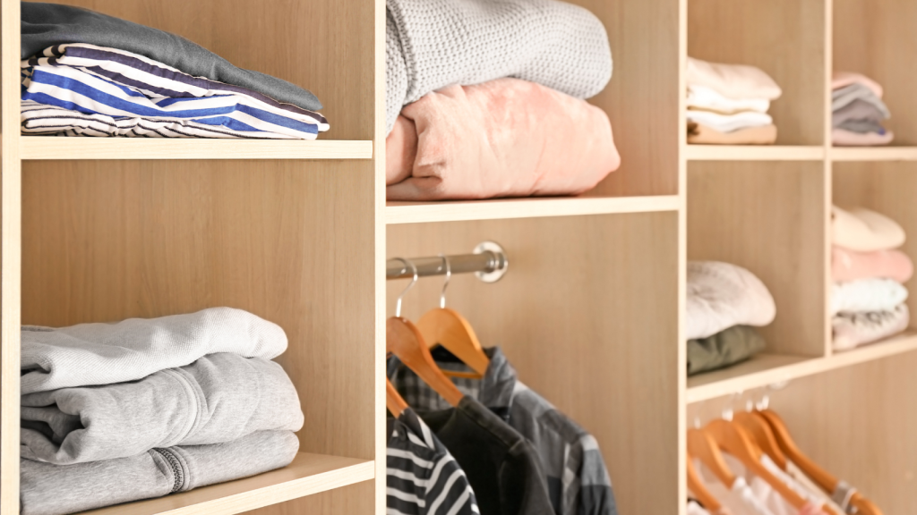 Open wooden closet shelves showcase a recent closet cleanout, with neatly folded clothes and several shirts hanging on wooden hangers. Closet cleanout guide